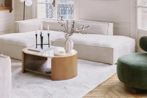 Tavolino con finitura in legno betulla colore, accanto a un divano bianco e una poltrona verde.