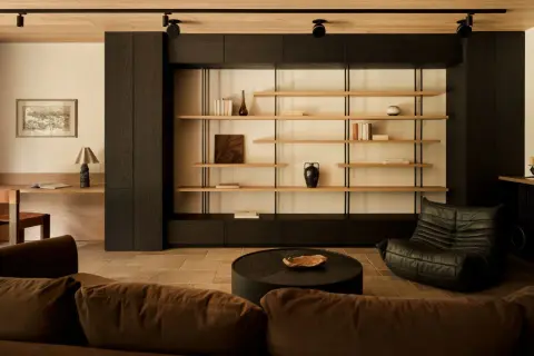 Un salotto con un divano marrone, una poltrona in pelle nera e uno scaffale aperto. Un angolo lettura con scrivania e sedia crea un piccolo giardino zen in casa.