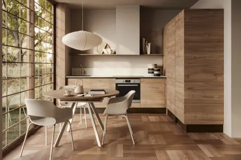 Ecco come arredare una cucina moderna: mobili in legno, tavolo rotondo con sedie bianche e grande finestra con vista sul verde.