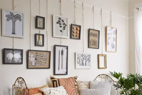 Una galleria di quadri appesi in modo originale con corde, tra cui una palma, conchiglie e piume.