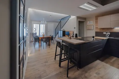 Elegante cucina soggiorno open space di 30 mq con isola nera, tavolo da pranzo in legno e scala moderna.
