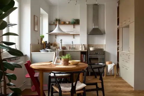 Accogliente cucina stile nordico con tavolo rotondo in legno, sedie in paglia e un grande ficus.