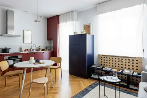 Interni di mini appartamenti con cucina rossa, tavolo rotondo, sedie in legno e un grande armadio blu.