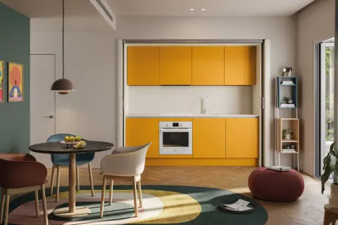Una cucina piccola con mobili gialli vivaci, un tavolo rotondo con sedie colorate e un tappeto circolare.