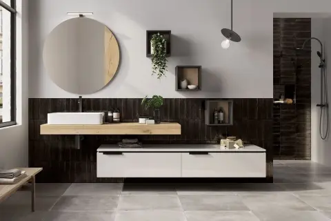 Bagno moderno con piastrelle nere verticali, lavabo bianco su mensola in legno, specchio rotondo e mobile sospeso. Idee bagno nero e legno per un look sofisticato.