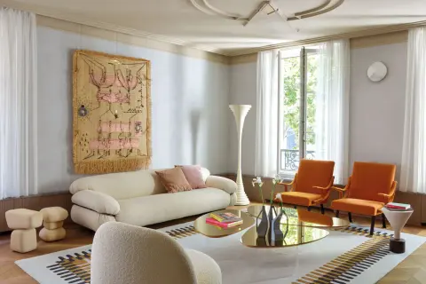 Soggiorno moderno con divano bianco, poltrone arancioni e arazzo colorato appeso alle pareti color crema.