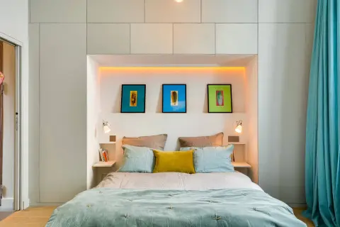 Letto moderno con nicchia illuminata, quadri colorati e comodini a scomparsa, perfetto per chi non ha spazio per i comodini.