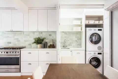 Soluzione elegante per come nascondere lavatrice e asciugatrice in una cucina moderna, integrate in una nicchia con ante a scomparsa.
