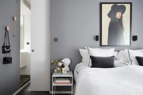 Pareti camera da letto grigia e bianche, con letto bianco, quadro di una donna con cappello e accessori appesi.