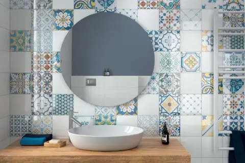 Bagno con lavabo su mobile in legno, specchio rotondo e pareti decorate con vivaci cementine bagno dai motivi geometrici e floreali.