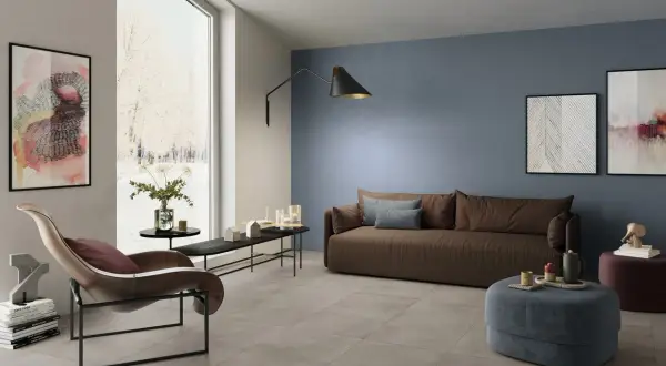 Soggiorno moderno con **pavimento grigio** e **pareti tortora** che creano un'atmosfera rilassante. Divano marrone, poltrona di design e opere d'arte completano l'arredo.