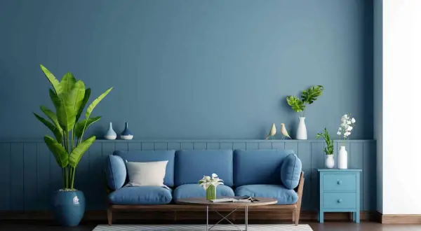 Soggiorno con divano blu e pareti color carta da zucchero. Piante verdi e decorazioni creano un'atmosfera rilassante.