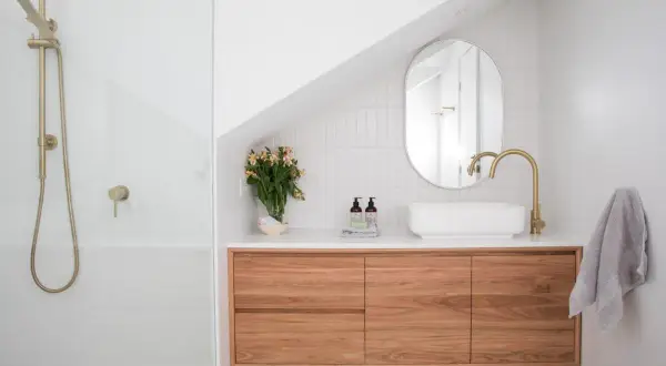 Un bagno moderno con doccia, mobile sospeso in legno, lavabo bianco e rubinetteria oro. Idee per come arredare un bagno con stile.