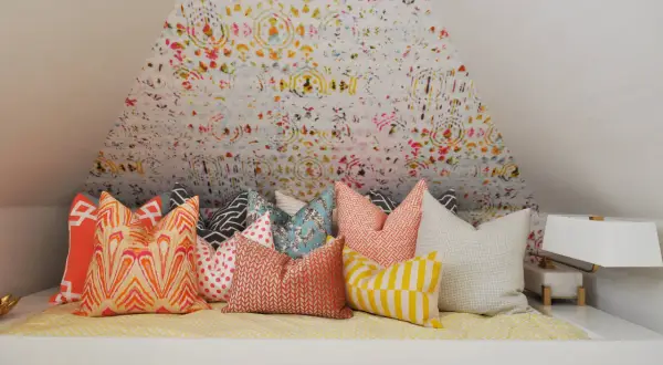 Un letto accogliente con tanti cuscini decorativi dai motivi vivaci e colorati, pronti per un riposo da sogno.