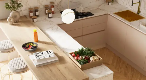 Top cucina con materiali innovativi: piano in legno chiaro, marmo bianco e oro, mobili color pesca. Frutta fresca, verdure e libri sul bancone.