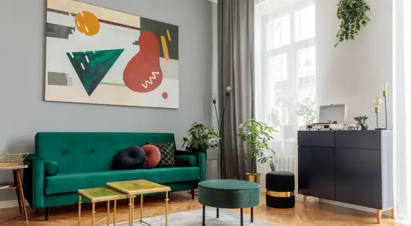 Soggiorno moderno con divano verde smeraldo, tavolini dorati e un quadro astratto. Un esempio di come abbinare i colori con stile.