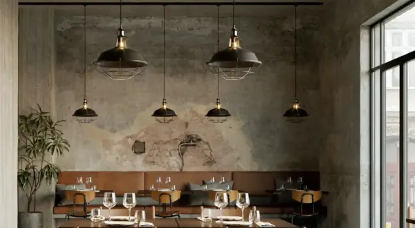 Un elegante lampadario a binario con sei luci industriali illumina un ristorante con pareti in cemento grezzo e divanetti in pelle marrone.