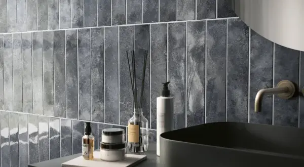 Un elegante bagno azzurro e grigio con piastrelle verticali, lavabo nero e rubinetto dorato.