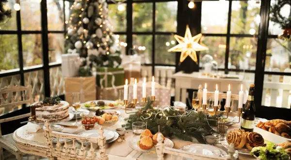 Tavola imbandita per Natale con torta, arrosti e candele. Un albero addobbato e regali creano l'atmosfera perfetta per le idee decorare la cucina per natale.