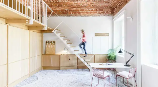 Soggiorno con soppalco a vista, soffitto in mattoni, scala bianca e una persona che sale. Arredamento moderno e minimalista.