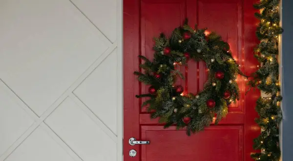 Un ingresso natalizio da sogno: una porta rossa con ghirlanda di pino, palline rosse e luci dorate per abbellire porta ingresso natale.