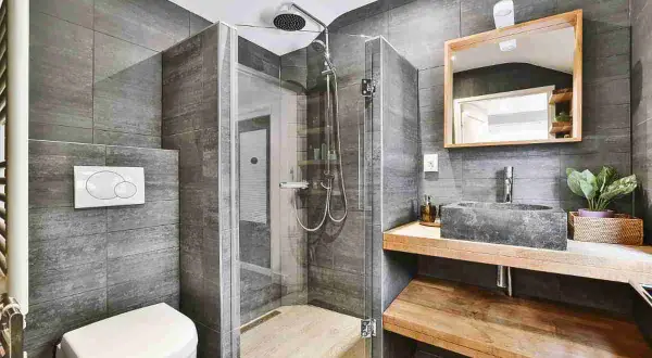 Bagno grigio chiaro e bianco con doccia in vetro, lavabo in pietra e specchio in legno.