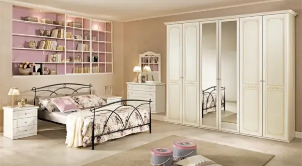 Camera da letto classica: letto in ferro battuto, armadio bianco con specchi, cassettiera e libreria a muro.