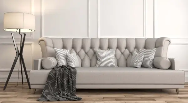 Divano imbottito beige con cuscini a righe grigie e una coperta scura. La lampada da terra nera completa l'arredamento, dimostrando che beige e grigio stanno bene insieme.