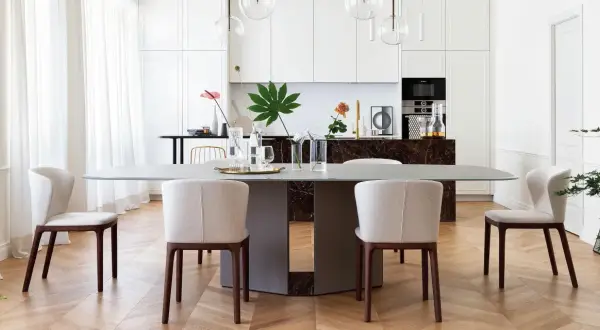 Un elegante tavolo da pranzo con sedie imbottite, parte di un progetto di casa in stile contemporaneo. La cucina moderna è visibile sullo sfondo.