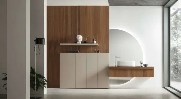 Un elegante bagno minimal con mobile sospeso in legno, lavabo bianco e specchio circolare retroilluminato.