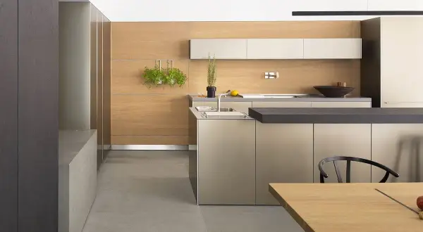 Cucina moderna con ante color tortora e pareti in legno chiaro. Un'isola centrale con piano scuro e un tavolo in legno completano l'ambiente.