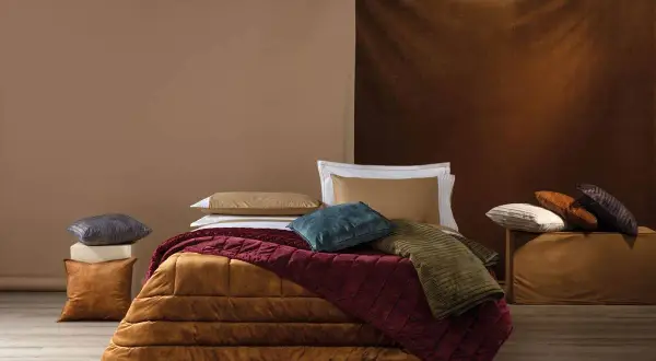 Come mettere il plaid sul letto: un letto accogliente con coperte e cuscini in tonalità calde e terrose.