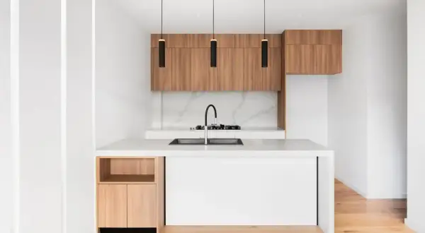 Cucine piccole particolari con isola bianca, pensili in legno e tre lampade nere sospese.
