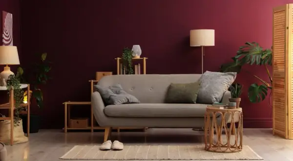 Soggiorno accogliente con divano grigio, piante verdi e pareti color vinaccia intenso.