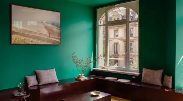 Un soggiorno moderno con pareti verde smeraldo, un quadro astratto, un divano basso in legno scuro e cuscini a quadri. I colori che stanno bene con il verde sono esaltati dal contrasto.