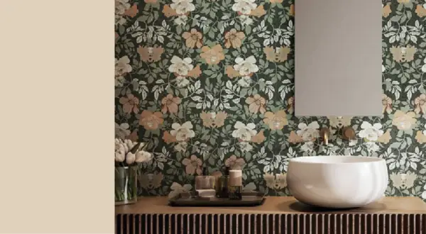 Bagno con carta da parati floreale su sfondo verde scuro, fiori bianchi e color sabbia. Lavabo bianco, specchio e rubinetteria dorata.