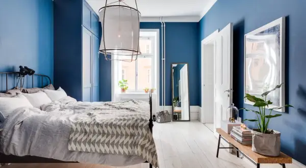 Accogliente camera da letto blu con letto matrimoniale, armadio blu e specchio a figura intera.