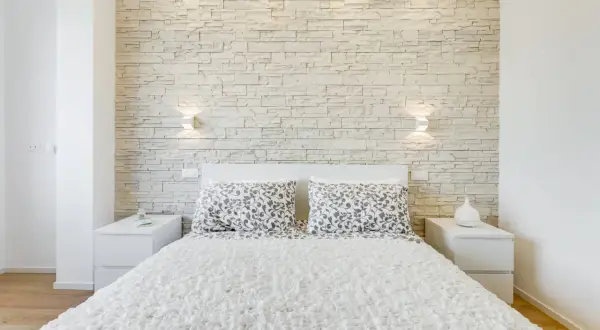 Accogliente camera da letto moderna con una suggestiva parete in pietra che fa da sfondo al letto.