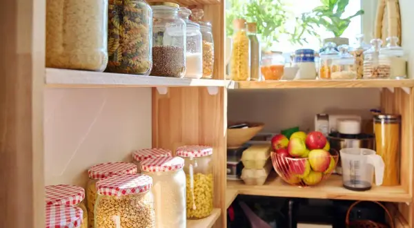 Dispensa organizzata con barattoli di pasta, riso, legumi e frutta fresca. Tutto in ordine per cucinare.