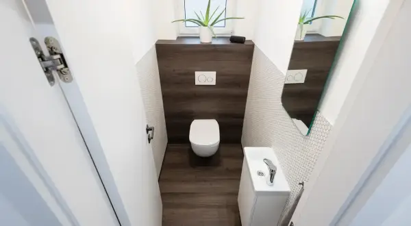 Bagno con wc e lavandino compatti, dimostra le dimensioni minime bagno solo wc. Specchio e pianta decorano lo spazio.