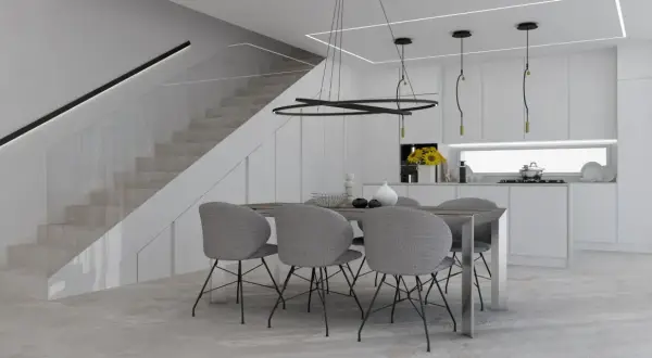 Un tavolo con sedie grigie in una moderna cucina bianca, con scala a vista e illuminazione minimalista. Perfette idee cucina bianca per un ambiente luminoso.