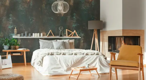 Camera da letto con carta da parati effetto materico e pittura chiara, letto bianco, camino e poltroncina gialla.