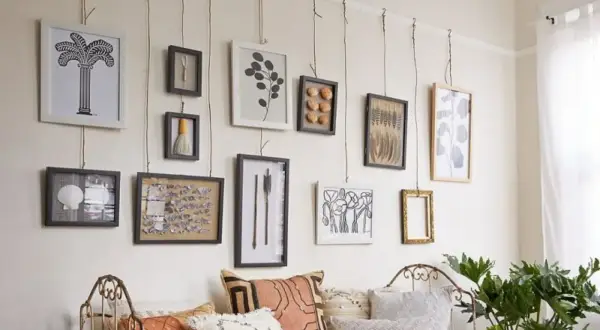 Una galleria di quadri appesi in modo originale con corde, tra cui una palma, conchiglie e piume.