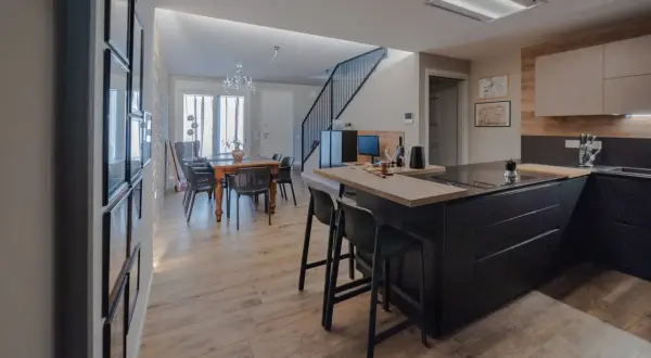 Elegante cucina soggiorno open space di 30 mq con isola nera, tavolo da pranzo in legno e scala moderna.