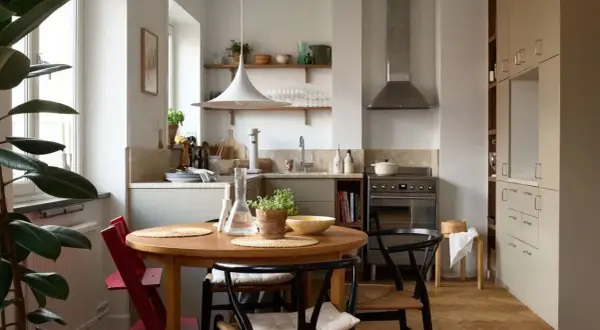 Accogliente cucina stile nordico con tavolo rotondo in legno, sedie in paglia e un grande ficus.