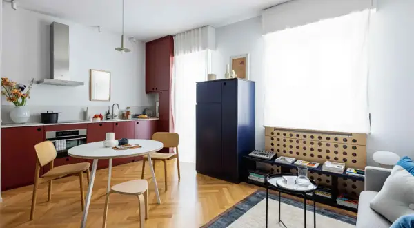 Interni di mini appartamenti con cucina rossa, tavolo rotondo, sedie in legno e un grande armadio blu.