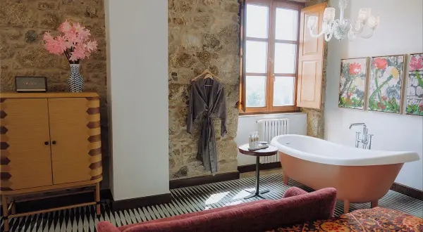 Un bagno rustico chic con vasca freestanding color pesca, pareti in pietra, un accappatoio appeso e un mobile in legno.