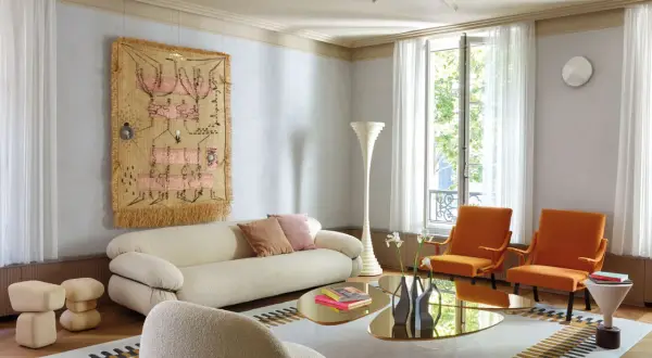 Soggiorno moderno con divano bianco, poltrone arancioni e arazzo colorato appeso alle pareti color crema.
