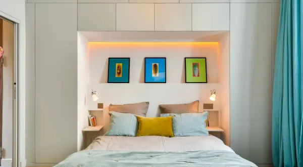 Letto moderno con nicchia illuminata, quadri colorati e comodini a scomparsa, perfetto per chi non ha spazio per i comodini.