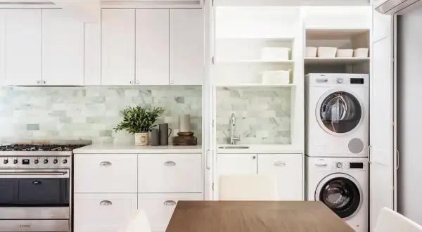 Soluzione elegante per come nascondere lavatrice e asciugatrice in una cucina moderna, integrate in una nicchia con ante a scomparsa.